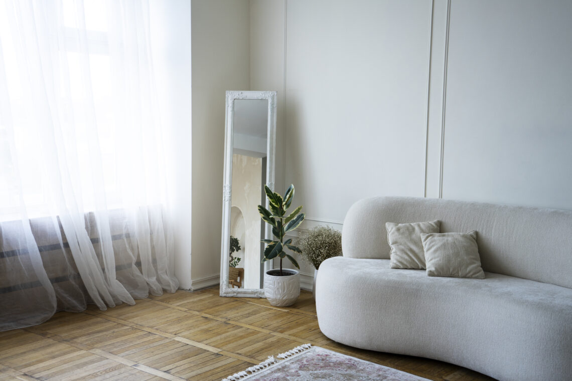 Sala de estar pequena com sofá cinza, espelho grande na parede e decoração minimalista em tons neutros