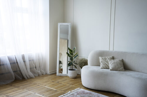 Sala de estar pequena com sofá cinza, espelho grande na parede e decoração minimalista em tons neutros