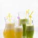Copos de suco detox coloridos, rodeados por frutas frescas, folhas de hortelã e gengibre, simbolizando saúde, frescor e bem-estar.