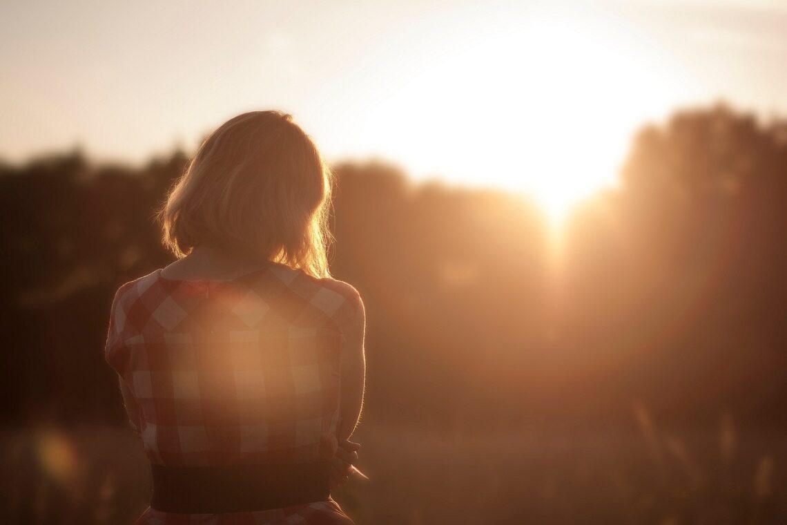 Mulher sorridente espreguiçando-se na cama ao amanhecer, com luz natural entrando pela janela, transmitindo leveza e bem-estar