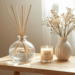 Difusor de ambiente em frasco de vidro com varetas de rattan sobre mesa decorada, em ambiente iluminado e aconchegante.